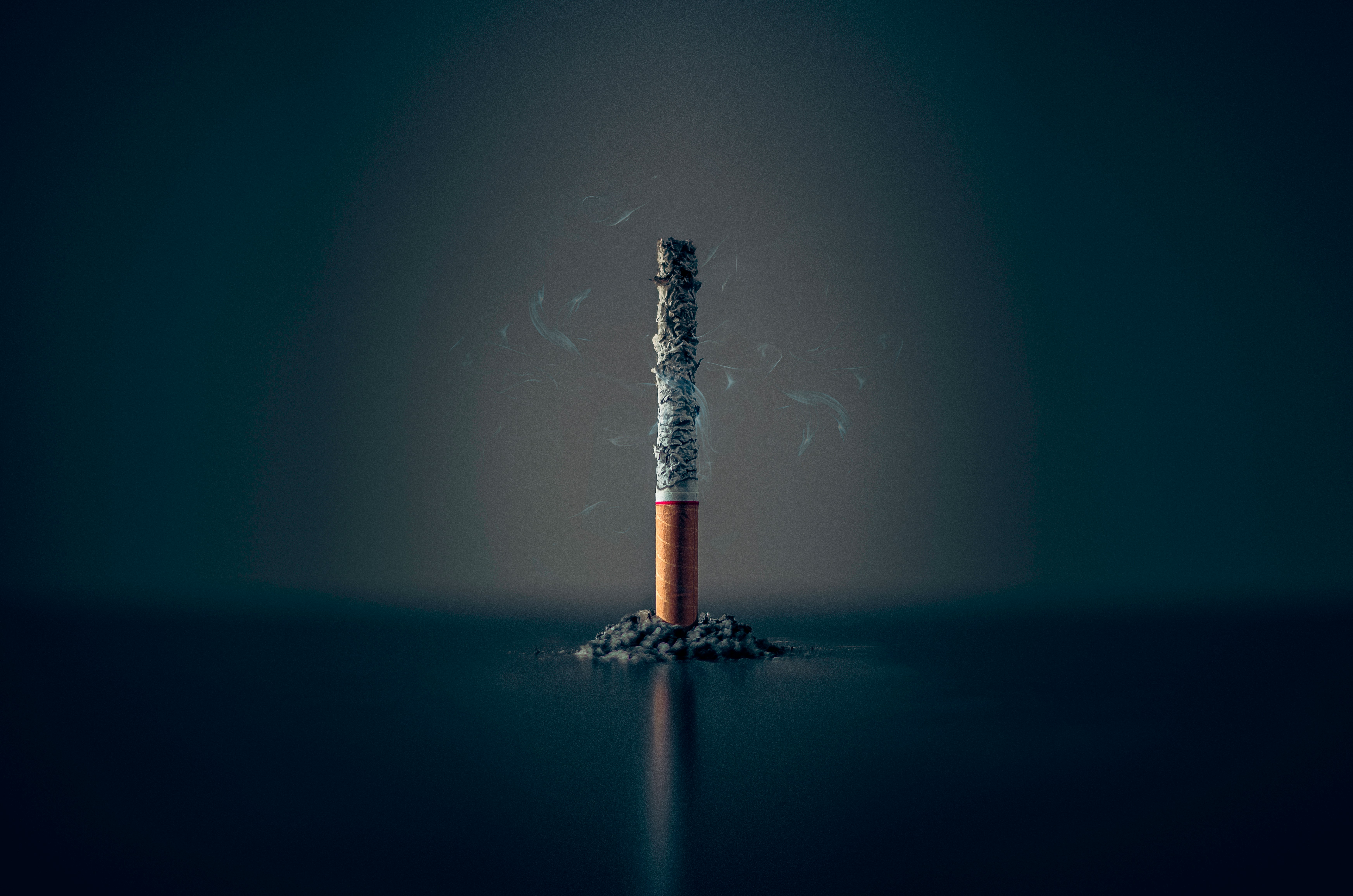Photographie illustrative d'une cigarette allumée consumant ses cendres sur fond sombre. Image libre de droits : Unsplash.